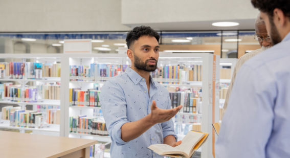 Three people discussing a book in a library setting.